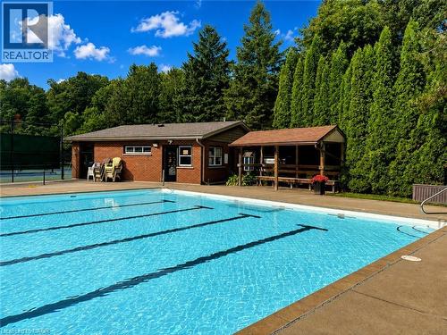 Outdoor swimming pool with integrated lane lines, concrete decking, brick building, and a covered wooden pavilion - 119 Sandy Ridge Place, Waterloo, ON - Outdoor With In Ground Pool With Deck Patio Veranda
