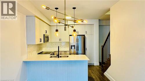 Modern kitchen featuring light-toned cabinetry, stainless steel appliances, a bar-height counter, and an angular chandelier - 1159 Lloyd Landing, Milton, ON - Indoor Photo Showing Kitchen With Double Sink