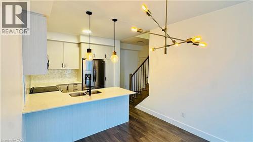 Modern open-concept kitchen and dining area featuring a blue-finished island with quartz countertop, stainless steel appliances, white cabinetry with hardware accents, pendant lighting, and warm wood- - 1159 Lloyd Landing, Milton, ON - Indoor Photo Showing Kitchen With Double Sink