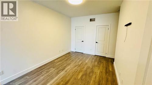 Wood-finish flooring, white walls, and two paneled doors with black hardware - 1159 Lloyd Landing, Milton, ON - Indoor Photo Showing Other Room