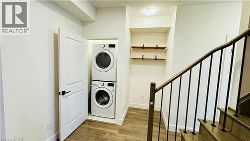 Integrated laundry appliances, wood-finish flooring, built-in shelving, wood handrail with black balusters, and recessed ceiling lighting - 1159 Lloyd Landing, Milton, ON - Indoor Photo Showing Laundry Room