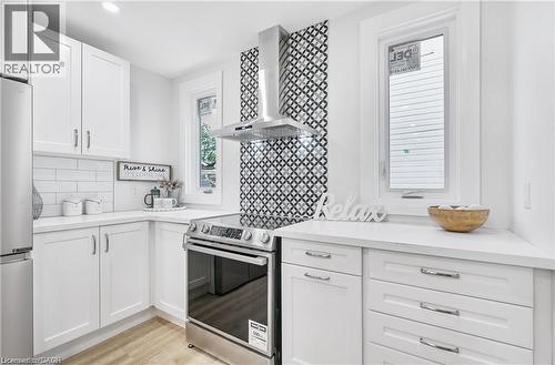 Modern kitchen featuring white cabinetry, light countertops, stainless steel appliances, a geometric patterned backsplash, and wood-finish flooring - 10 Comet Avenue Unit# #1 (Main), Hamilton, ON - Indoor Photo Showing Kitchen