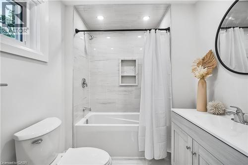 Bathroom featuring a tiled shower and tub combination with a built-in niche, a single vanity with a white countertop, and a circular wall mirror - 10 Comet Avenue Unit# #1 (Main), Hamilton, ON - Indoor Photo Showing Bathroom