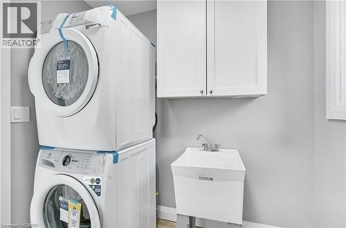 Laundry area featuring a stackable washer and dryer, white shaker-style cabinetry, and a utility sink with a chrome faucet - 10 Comet Avenue Unit# #1 (Main), Hamilton, ON - Indoor Photo Showing Laundry Room