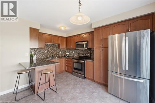 Well-appointed kitchen featuring wood-finish cabinetry, stainless steel appliances, a breakfast bar, patterned backsplash, and tile flooring - 171 Chase Crescent, Cambridge, ON - Indoor Photo Showing Kitchen With Stainless Steel Kitchen