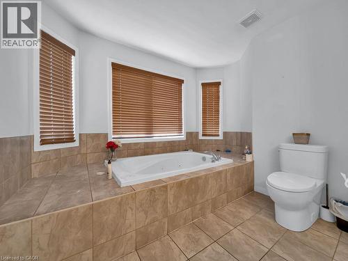 Built-in jetted tub surrounded by large format tile, complemented by a white toilet - 227 Baldwin Drive Unit# Main, Cambridge, ON - Indoor Photo Showing Bathroom