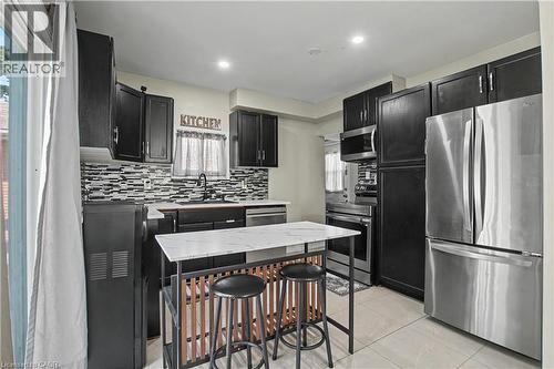 Modern kitchen featuring dark cabinetry, stainless steel appliances, a mosaic tile backsplash, and a central island with a stone-finish countertop - 16 Mercer Road, Cambridge, ON - Indoor