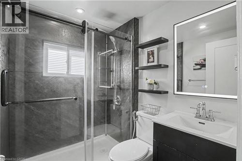 Frameless glass shower enclosure with sliding door, dark stone-finish shower walls, window with blinds, illuminated mirror, and floating shelving - 16 Mercer Road, Cambridge, ON - Indoor Photo Showing Bathroom