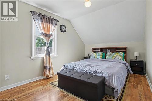 Sloped ceiling bedroom featuring wood-finish flooring, a double-hung window, and a built-in headboard with shelving - 16 Mercer Road, Cambridge, ON - Indoor Photo Showing Bedroom