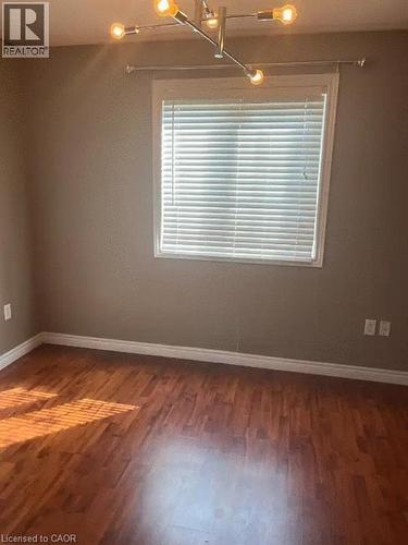 Room featuring wood-finish flooring, a window with blinds, a white window frame, and a modern ceiling light fixture - 4000 Medland Drive, Burlington, ON - Indoor Photo Showing Other Room