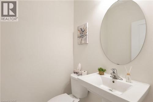 Wall-mounted rectangular sink with chrome faucet, circular mirror, and white toilet - 285 Broadacre Drive, Kitchener, ON - Indoor Photo Showing Bathroom