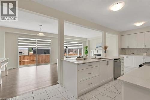 Open-concept design featuring a central kitchen island with an integrated sink, white cabinetry with silver hardware, white tile flooring, and wood-finish flooring in the adjoining space - 285 Broadacre Drive, Kitchener, ON - Indoor Photo Showing Kitchen With Double Sink