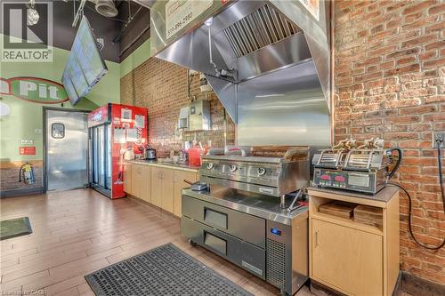 Commercial kitchen area featuring an exposed brick wall, stainless steel griddle with exhaust hood, and light wood-finish cabinetry - 589 Fairway Road S, Kitchener, ON 