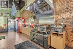 Commercial kitchen area featuring an exposed brick wall, stainless steel griddle with exhaust hood, and light wood-finish cabinetry - 