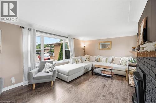Spacious living area featuring expansive windows, wood-finish flooring, and a painted brick-surround fireplace with a wood mantel - 481 Upper Gage Avenue, Hamilton, ON - Indoor Photo Showing Living Room With Fireplace