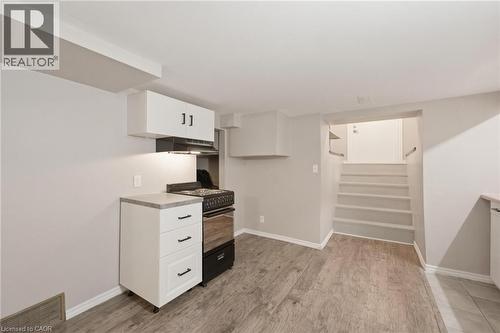 Basement kitchen area featuring a freestanding black and stainless steel range, range hood, white upper and lower cabinetry with dark hardware, a light-toned countertop, and private entrance - 481 Upper Gage Avenue, Hamilton, ON - Indoor Photo Showing Other Room