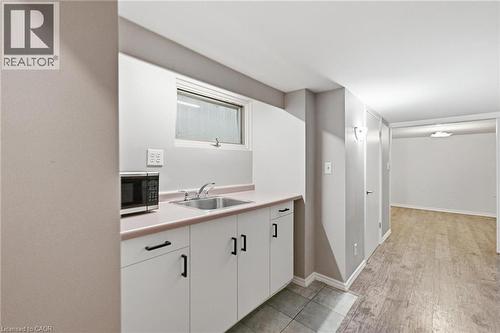 Basement kitchen area featuring a sink, microwave, white cabinetry with dark hardware, light-toned countertop, and a large window - 481 Upper Gage Avenue, Hamilton, ON - Indoor Photo Showing Other Room