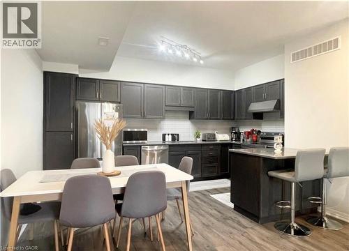 Kitchen featuring dark wood-finish cabinetry, stainless steel appliances, a tile backsplash, and a breakfast bar with a solid surface countertop - 17 Visionary Avenue, Kitchener, ON - Indoor