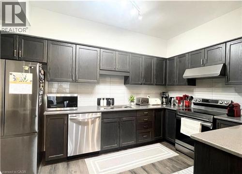 Kitchen featuring dark wood-finish cabinetry, stainless steel appliances, a white subway tile backsplash, light-toned countertops, and wood-finish flooring - 17 Visionary Avenue, Kitchener, ON - Indoor Photo Showing Kitchen With Double Sink With Upgraded Kitchen