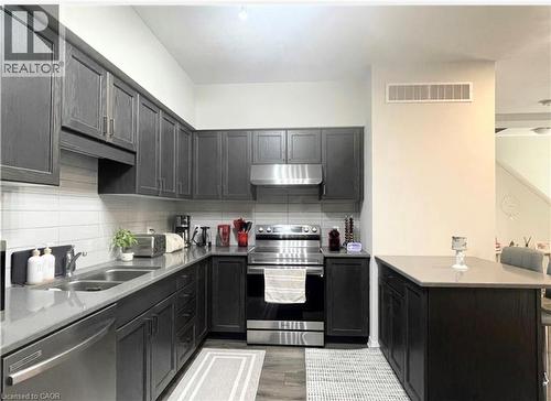 Kitchen featuring dark wood-finish cabinetry, light stone countertops, white subway tile backsplash, stainless steel appliances, and a built-in kitchen island - 17 Visionary Avenue, Kitchener, ON - Indoor Photo Showing Kitchen With Double Sink With Upgraded Kitchen