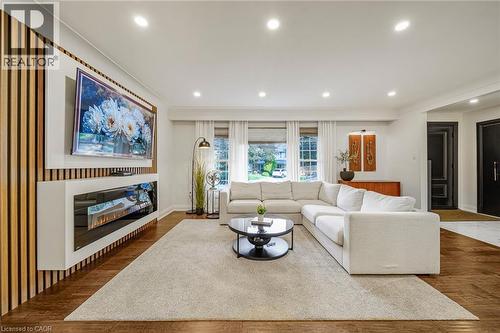 Recessed lighting, wood-finish flooring, built-in electric fireplace, wall-mounted display unit, and multiple windows with window treatments - 24 Garvey Crescent, Hamilton, ON - Indoor Photo Showing Living Room With Fireplace