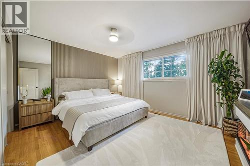 Wood-finish flooring with a light area rug, featuring a window with white trim, and a textured accent wall - 24 Garvey Crescent, Hamilton, ON - Indoor Photo Showing Bedroom