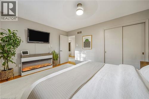 Hardwood-style flooring, contemporary ceiling light fixture, white interior door, sliding closet doors, and a linear electric fireplace - 24 Garvey Crescent, Hamilton, ON - Indoor Photo Showing Bedroom