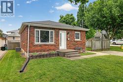 Brick exterior featuring a white entry door, multiple windows with white trim, and a concrete pathway leading to the entrance - 
