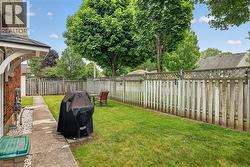 Enclosed backyard featuring a manicured lawn, a concrete pathway, a wood picket fence with lattice top, and mature trees - 