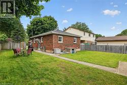 Spacious rear yard featuring an extensive lawn, mature trees, concrete pathway, and a brick exterior - 