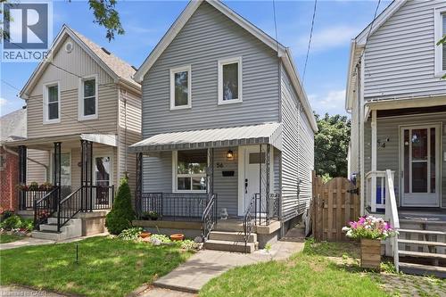 Light gray horizontal siding exterior with a pitched roof, front porch with an awning, black wrought iron railing, and concrete steps - 56 Harmony Avenue, Hamilton, ON - Outdoor With Deck Patio Veranda With Facade