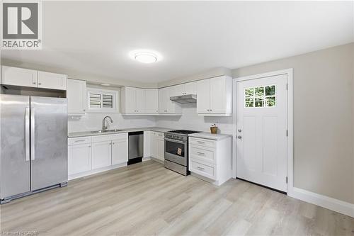White cabinetry, stainless steel appliances, light wood-finish flooring, white subway tile backsplash, and a paneled entry door with divided lites - 56 Harmony Avenue, Hamilton, ON - Indoor Photo Showing Kitchen