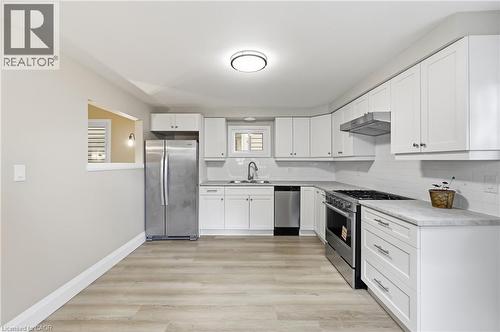Modern kitchen featuring white cabinetry with ample storage, stainless steel appliances including a gas range and refrigerator, white subway tile backsplash, light wood-finish flooring, and a function - 56 Harmony Avenue, Hamilton, ON - Indoor Photo Showing Kitchen With Stainless Steel Kitchen With Upgraded Kitchen