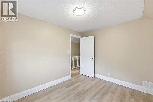 Neutral wall finish, wood-finish flooring, white trim, and a modern flush-mount light fixture - 56 Harmony Avenue, Hamilton, ON - Indoor Photo Showing Other Room