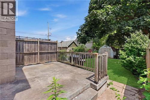 Spacious concrete patio with wood-finish railing and gated entry, adjoining a manicured lawn with mature landscaping and established trees - 56 Harmony Avenue, Hamilton, ON - Outdoor