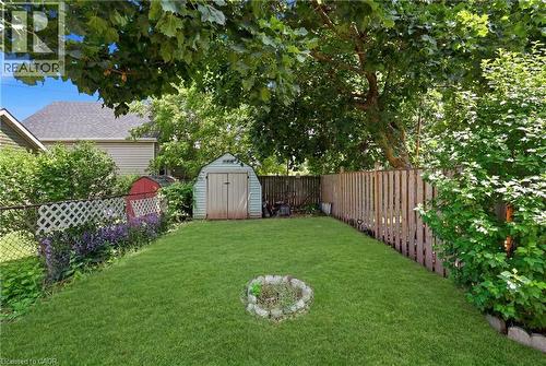 Expansive backyard featuring a lush, manicured lawn anchored by mature shade trees, wooden privacy fencing, a storage shed, and a fire pit ring—ideal for outdoor entertaining and recreation - 56 Harmony Avenue, Hamilton, ON - Outdoor