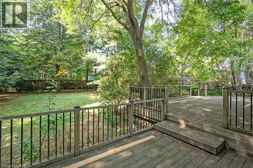 Spacious wooden deck with black metal balusters and built-in steps, overlooking a manicured lawn surrounded by mature trees and a privacy fence - 4189 Inglewood Drive, Burlington, ON - Outdoor