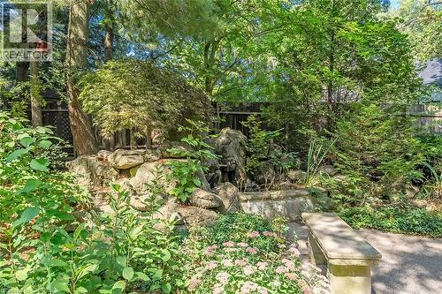 Lush garden landscaping featuring diverse foliage, a rock water feature, a stone bench, and mature trees - 4189 Inglewood Drive, Burlington, ON - Outdoor