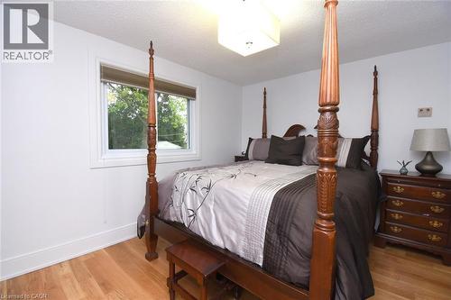 Master bedroom with four-poster wood bed frame, wood-finish flooring, and natural light from a large casement window - 374 Brigadoon Drive, Hamilton, ON - Indoor Photo Showing Bedroom