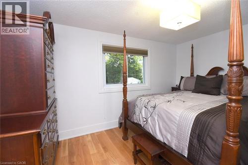 Bright secondary bedroom featuring a four-poster bed frame with carved wood finials, warm wood-finish flooring, and a large double-hung window with white trim providing natural light - 374 Brigadoon Drive, Hamilton, ON - Indoor Photo Showing Bedroom
