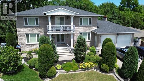 Two-story stone exterior featuring a covered front entry with columns, a second-story balcony with an ornate railing, a double-car garage, and a landscaped front yard with decorative shrubs and paving - 35 Glen Park Court, Hamilton, ON - Outdoor With Facade