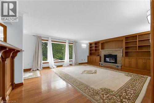 Wood-finish flooring throughout, featuring a stone fireplace with a built-in wood surround, extensive built-in shelving, and large windows - 35 Glen Park Court, Hamilton, ON - Indoor Photo Showing Other Room With Fireplace