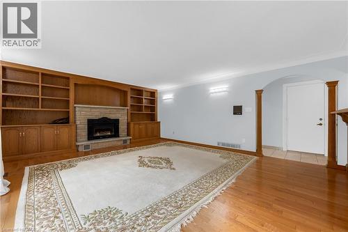 Wood-finish flooring throughout, integrated built-in shelving, stone-clad fireplace, and arched doorway with decorative wood columns - 35 Glen Park Court, Hamilton, ON - Indoor With Fireplace