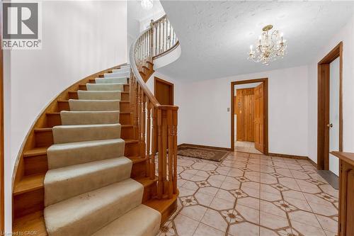 Curved staircase with wood treads and carpet runners, detailed wood banister, chandelier lighting, and patterned tile flooring - 35 Glen Park Court, Hamilton, ON - Indoor Photo Showing Other Room