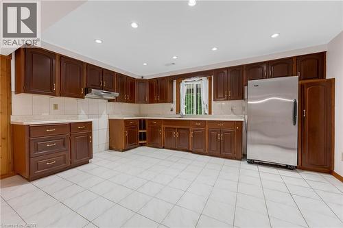 Spacious kitchen featuring extensive dark wood cabinetry, white tile flooring, a tile backsplash, recessed lighting, and a stainless steel refrigerator - 35 Glen Park Court, Hamilton, ON - Indoor Photo Showing Kitchen