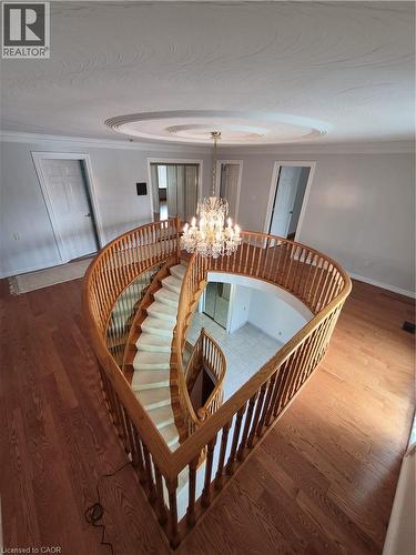 Grand spiral staircase with wood banister, wood-finish flooring, and a crystal chandelier - 35 Glen Park Court, Hamilton, ON - Indoor