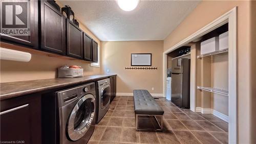 Dedicated laundry room featuring dual front-load washers and dryers, dark cabinetry with ample storage, tile flooring, and a built-in bench - 913 Valebrook Court, Kitchener, ON - Indoor Photo Showing Laundry Room