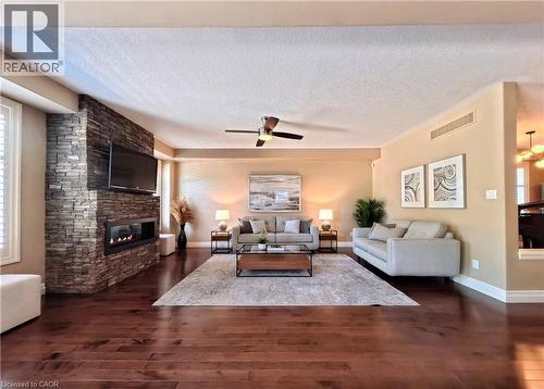 Spacious living room showcasing rich wood-finish flooring, a striking brick fireplace with integrated flat-screen television, and ceiling fan - 913 Valebrook Court, Kitchener, ON - Indoor Photo Showing Living Room With Fireplace