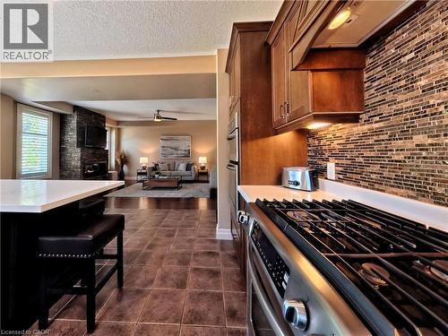 Stainless steel gas range with a tile backsplash, wood cabinetry, and a kitchen island with seating - 913 Valebrook Court, Kitchener, ON - Indoor Photo Showing Kitchen