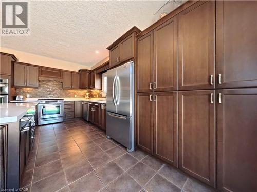Kitchen featuring extensive wood-finish cabinetry, stainless steel appliances, a tile backsplash, and solid surface countertops - 913 Valebrook Court, Kitchener, ON - Indoor Photo Showing Kitchen